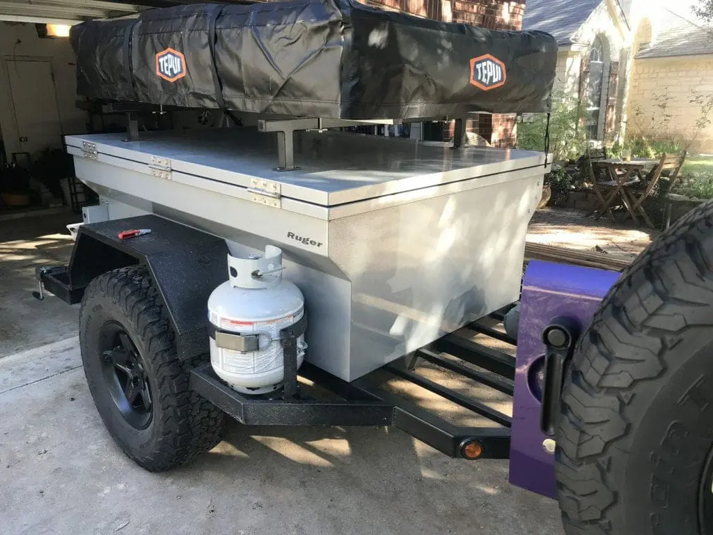 rooftop tent mounted on a Ruger off road trailer towed by a Jeep wrangler.