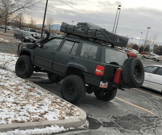 lifted Jeep with rooftop tent mounted on roof rack.